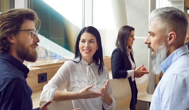 Group of men and women standing by an office window, talking, discussing work and sharing opinions on business management.