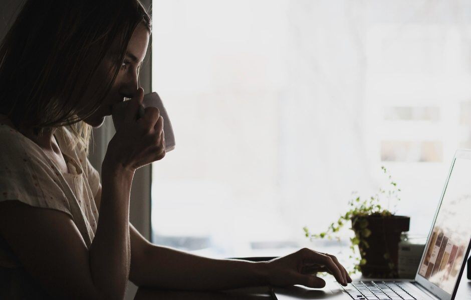 woman drinking from a mug close to window