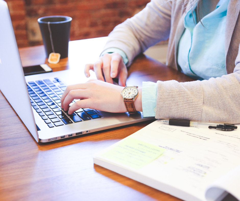 hands on a laptop surrounded by a book and mug