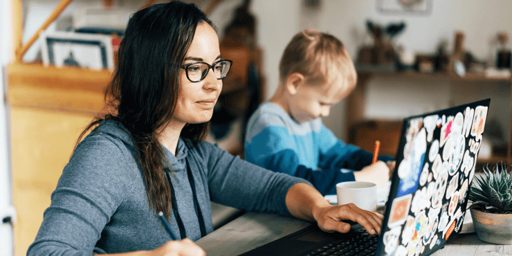 A mom taking an online college course at home with her son sitting beside her, drawing pictures in a notebook.