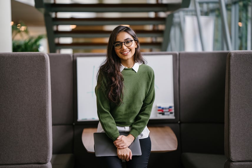 Portrait of a young MBA student smiling as she leans in a discussion booth in her campus.