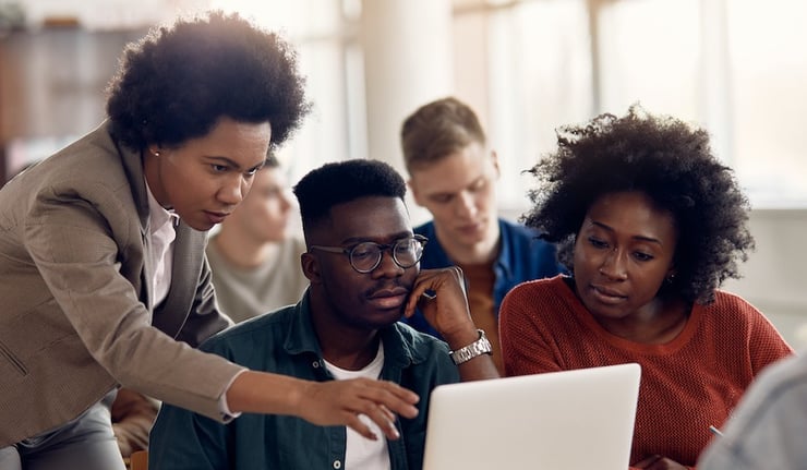 Adult students looking at their laptop and teacher explaining an assignment