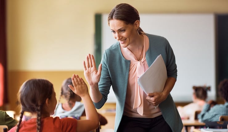 Happy teacher and schoolgirl giving high five during class at school.