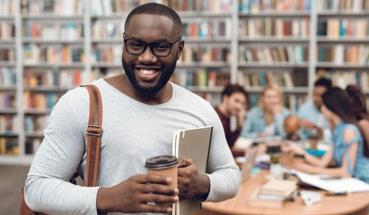 Group of ethnic multicultural students in library. Black guy with notes and coffee