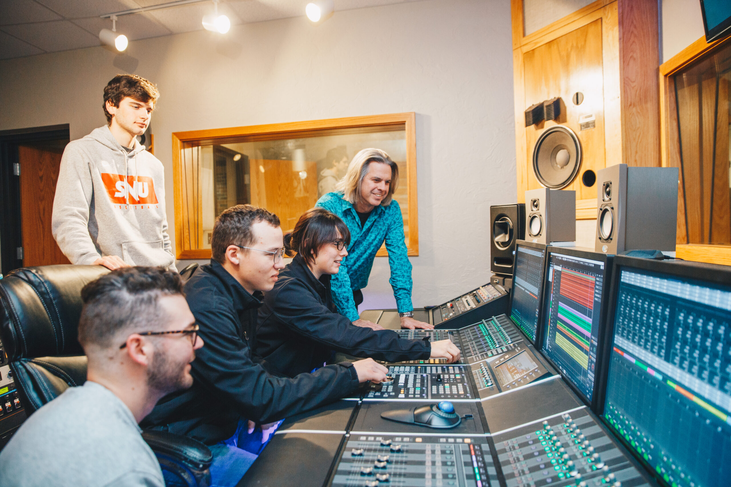 Students working together in the SNU recording studio while sitting in front of a control board